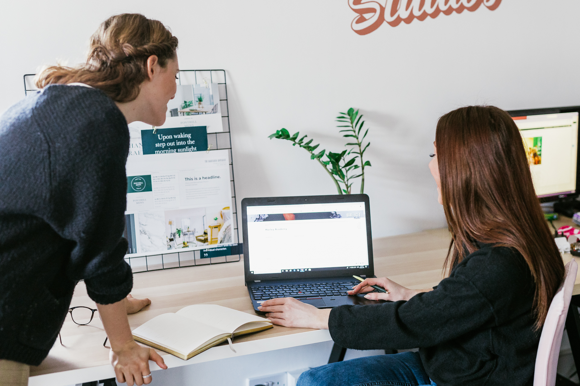 Two members of the Barefaced Studio's team working in the marketing office comparing notes while looking at work on the same laptop.