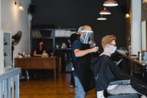 A picture of Em cutting a customer's hair with social distance regulations as he wears a mask and face visor.